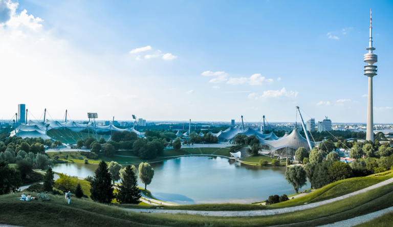 Daytime panoramic view of Munich Olympiapark with Olympic Tower tent roof structures and lake from the hill