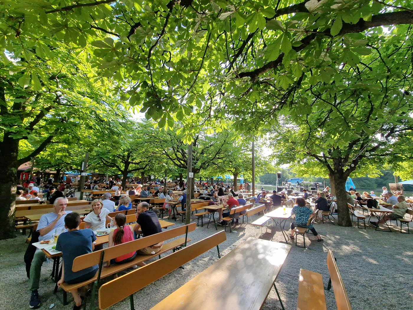 Families seated under chestnut trees at Michaeligarten beer garden beside Ostparksee in Munich