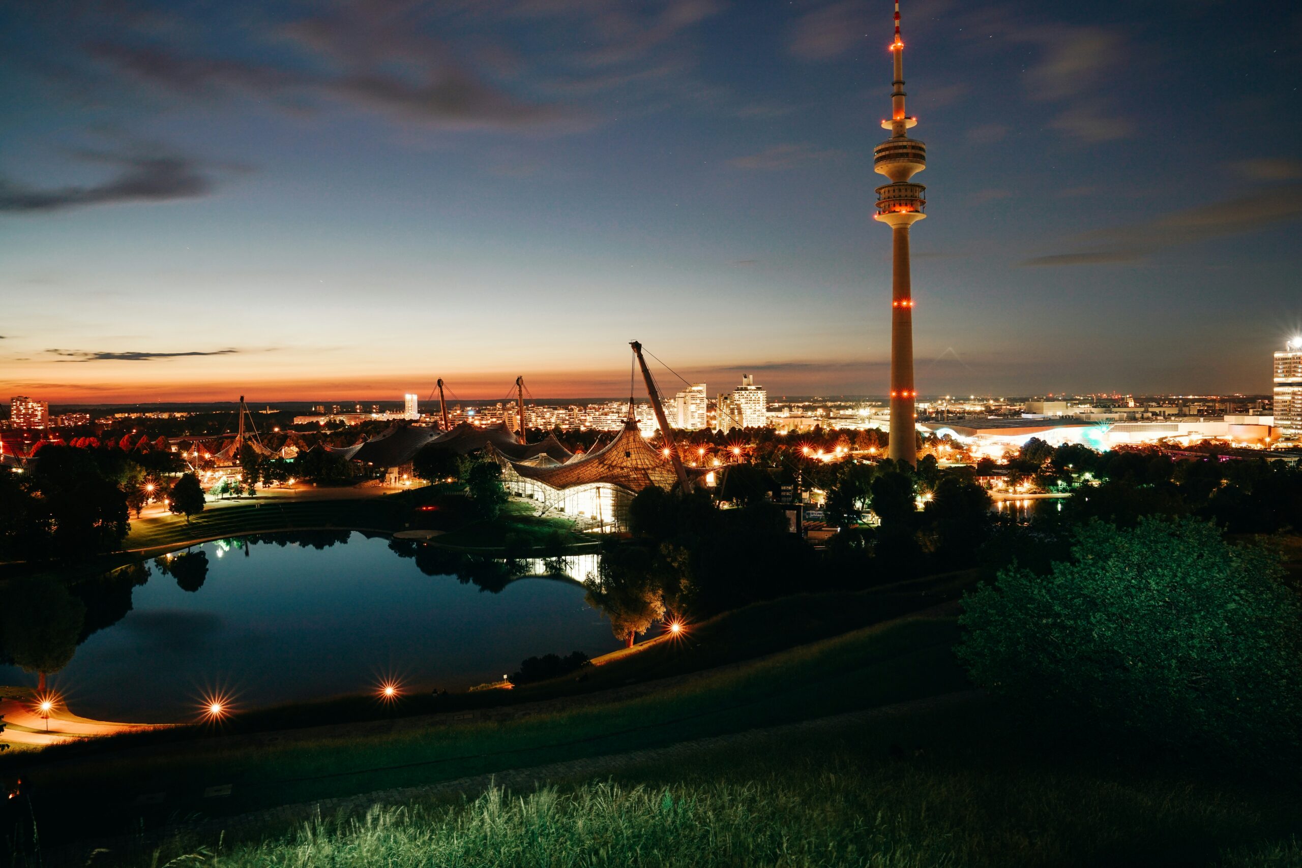 Olympiapark Munich at dusk with Olympiaturm and the Olympic Lake